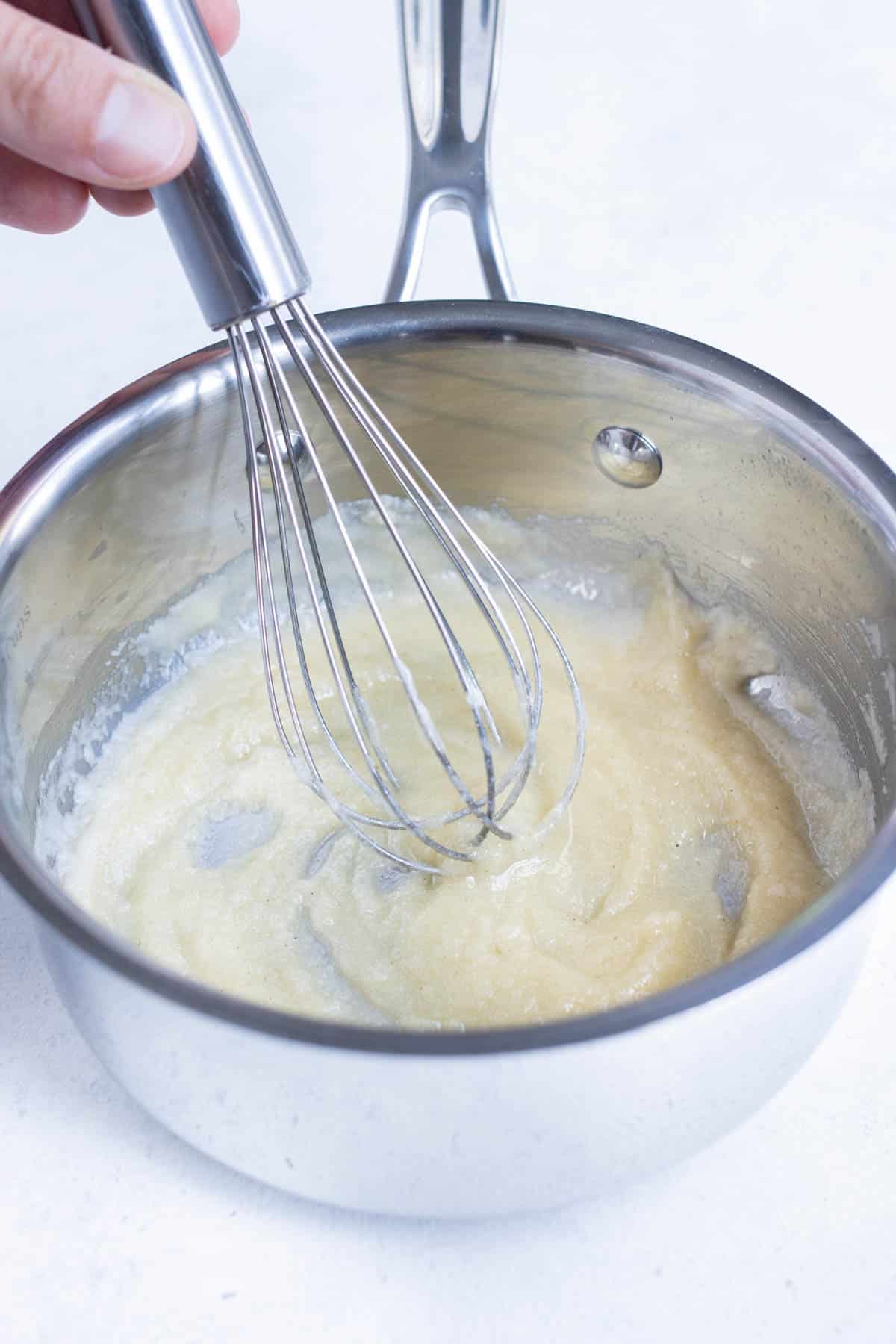 A whisk stirs the roux in a pan.