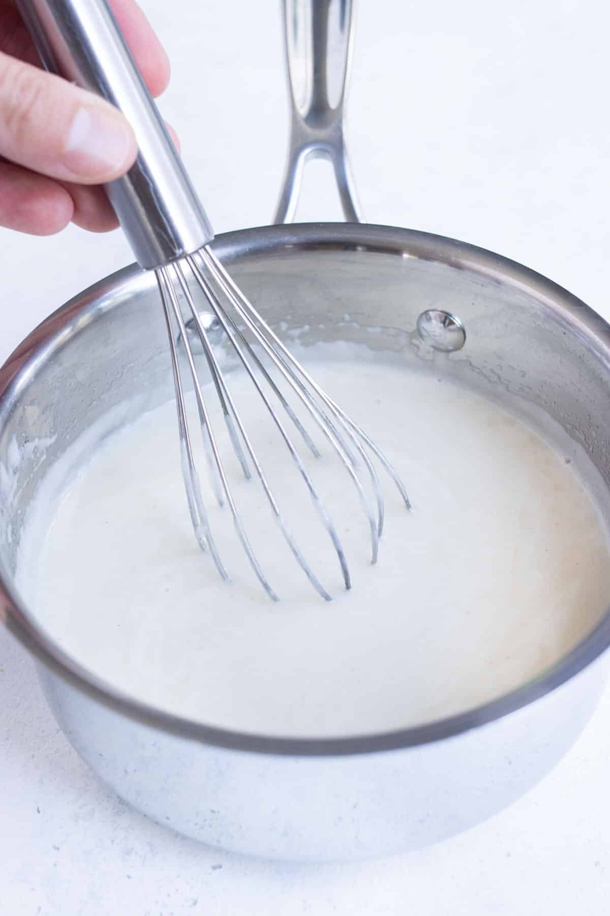 A whisk stirs in milk to the gravy mixture.