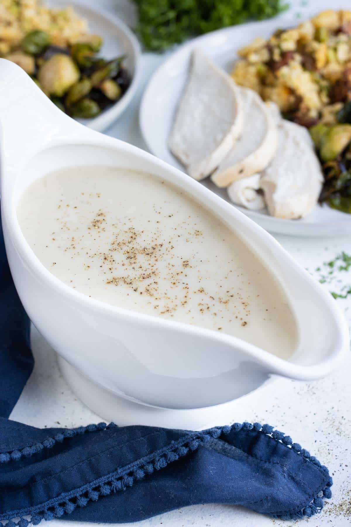 A gravy boat full of make-ahead gravy next to turkey and stuffing.