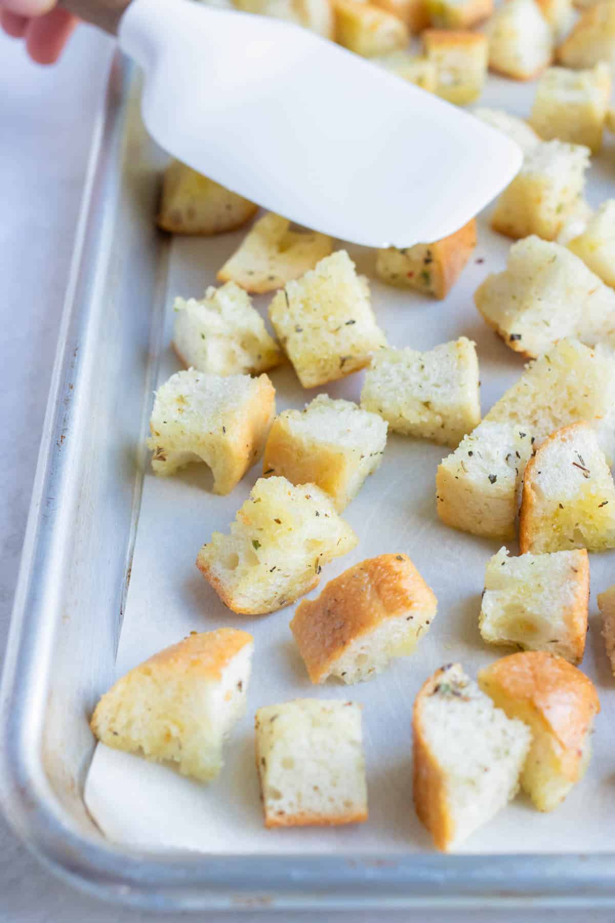 Bread cubes are spread out on a baking sheet before baking.