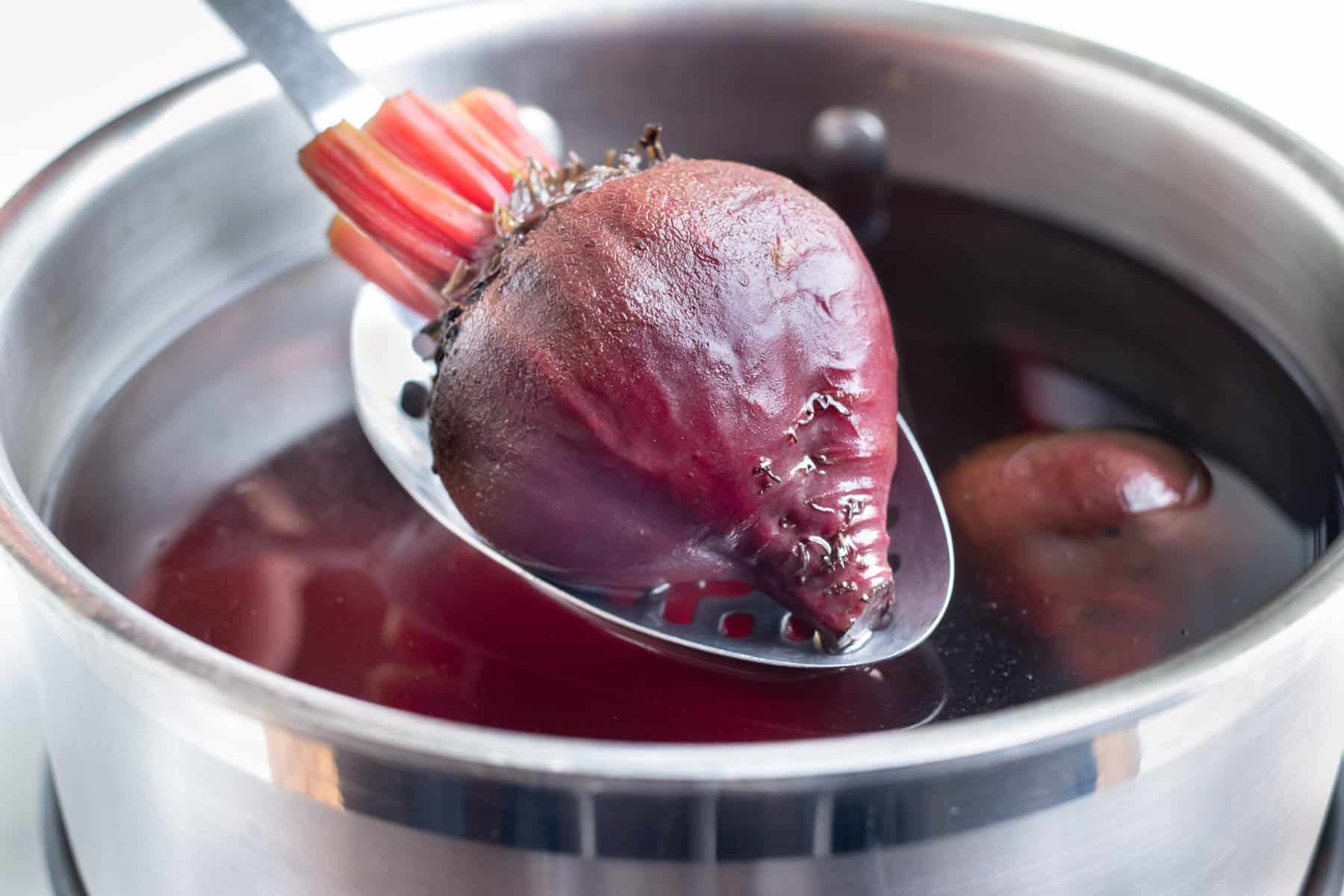 A metal spoon lifts the boiled beet from the pot.