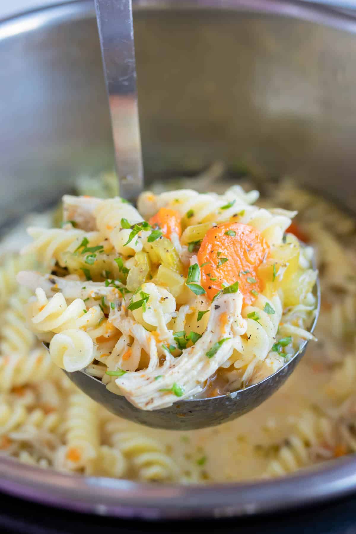 Pressure cooker chicken noodle soup is served with a metal ladle.