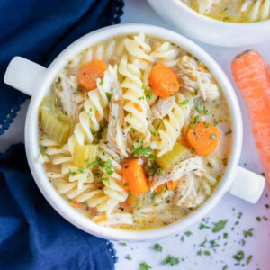 A carrot is placed beside a big bowl of healthy chicken noodle soup.