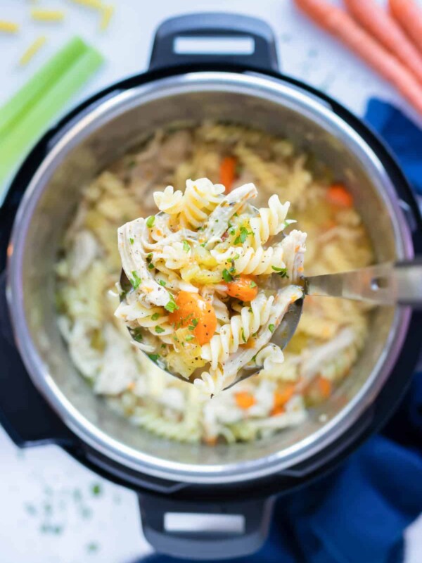 Healthy instant pot chicken noodle soup is lifted out of the instant pot with a ladle.