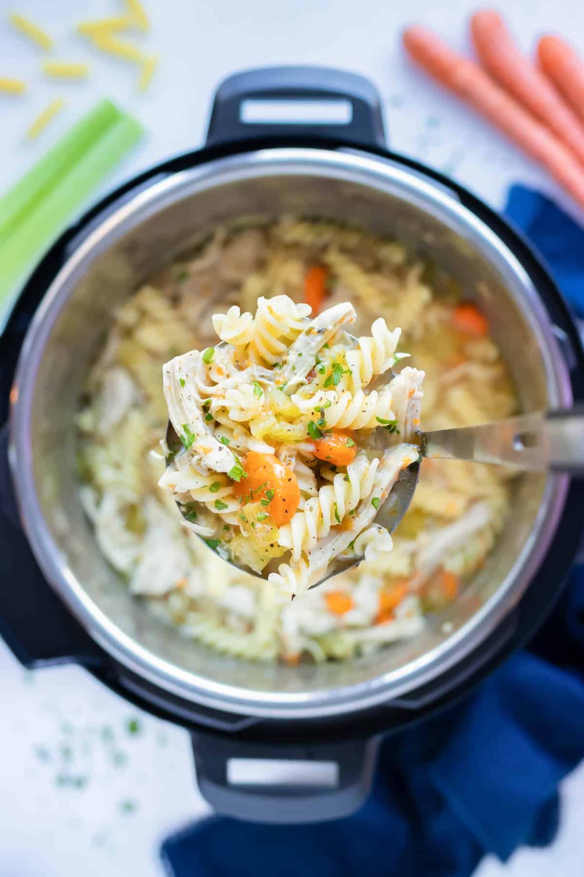 Healthy instant pot chicken noodle soup is lifted out of the instant pot with a ladle.