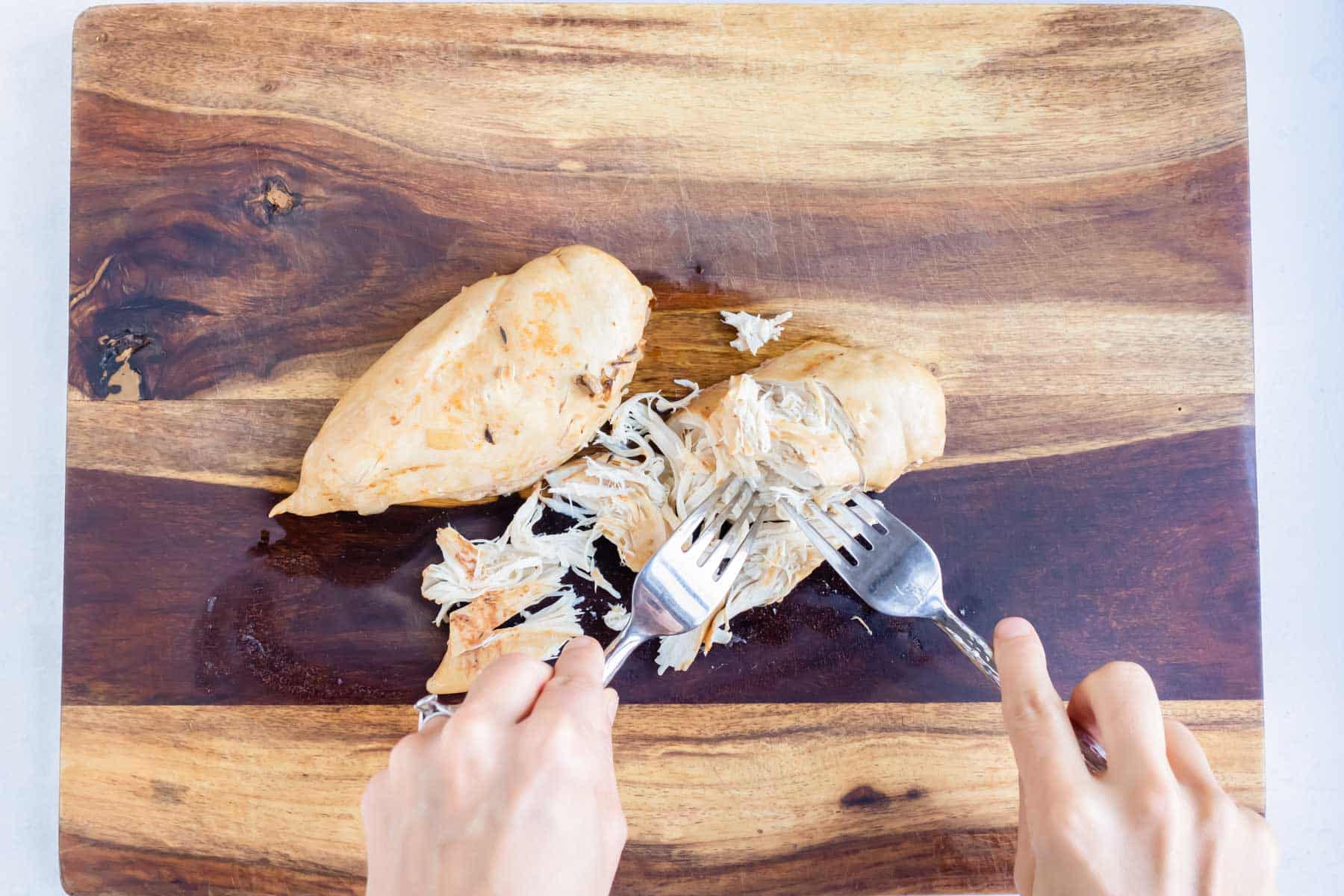 Cooked chicken is removed and shredded on a cutting board.