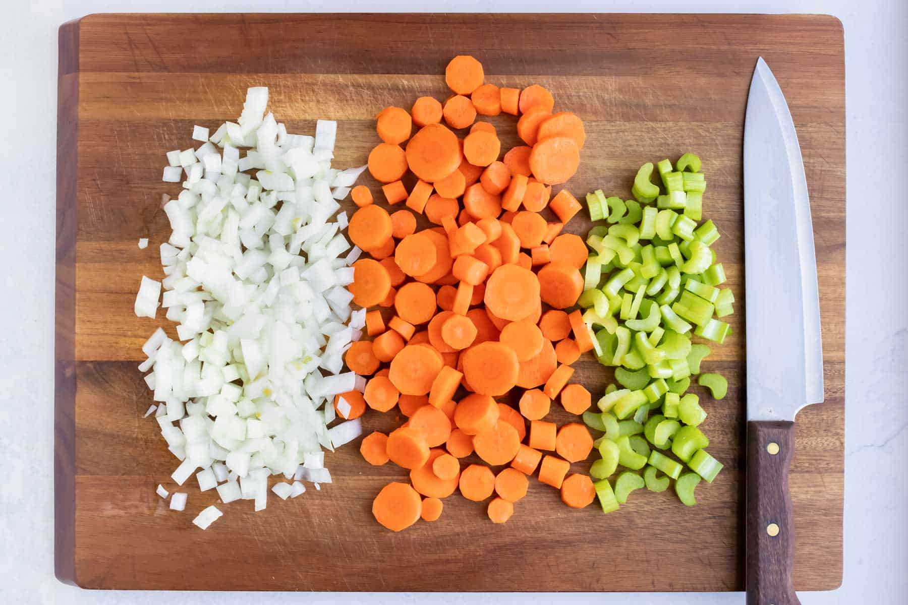 Onions, carrots, and celery are diced on a cutting board.