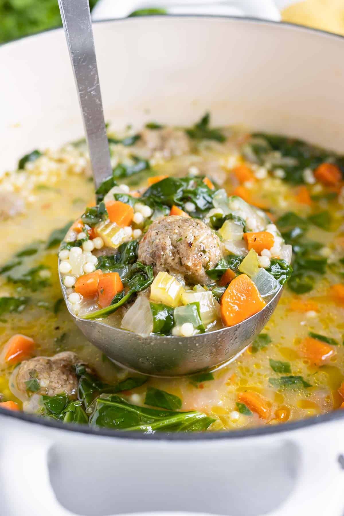 A ladle scooping up Italian wedding soup from a white Dutch oven.