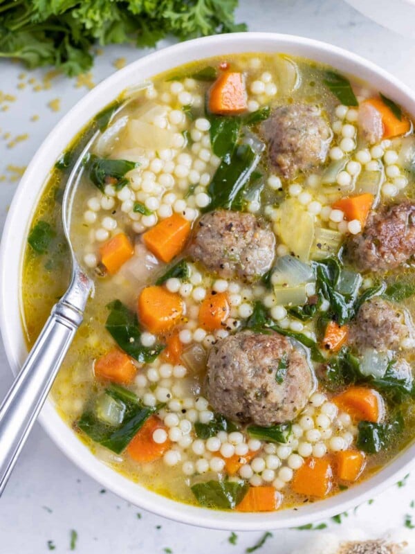 Italian wedding soup recipe in a white bowl with a spoon in it.