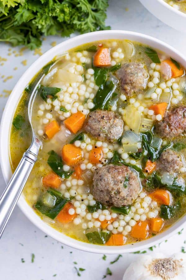 Italian wedding soup recipe in a white bowl with a spoon in it.