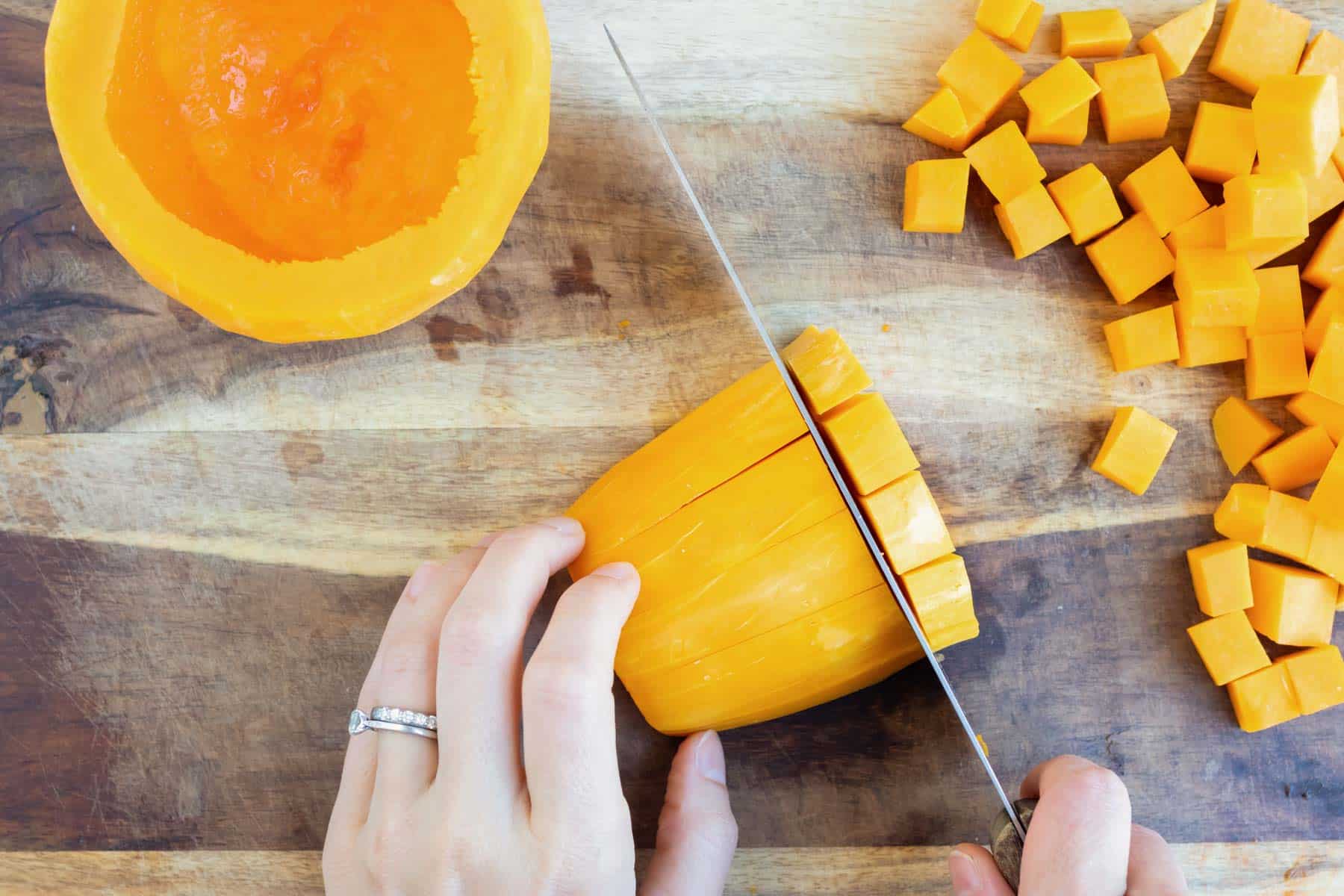 A large knife cuts butternut squash into cubes.