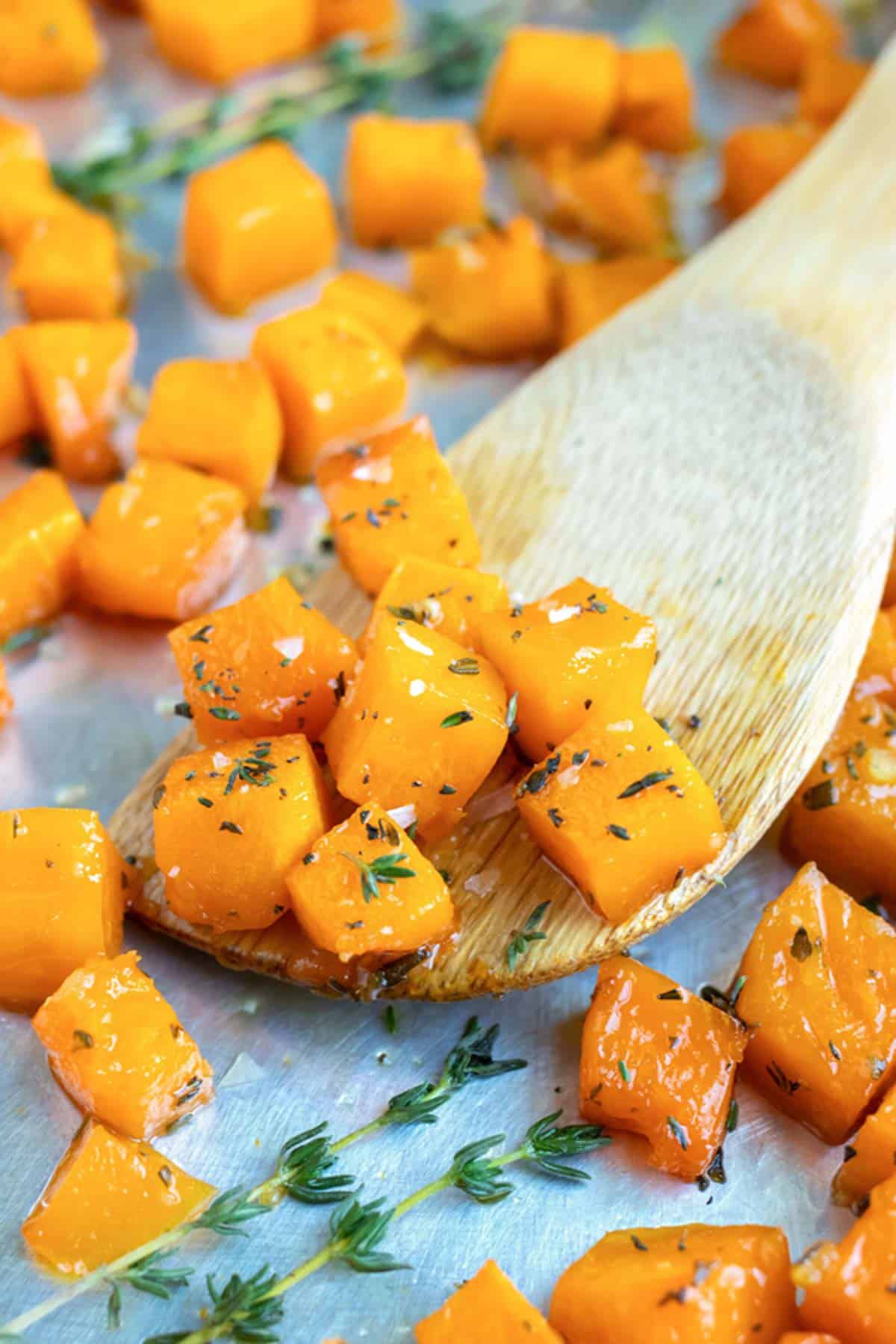 A wooden spatula picking up roasted butternut squash cubes with thyme.