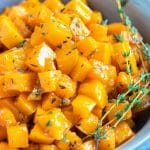 A serving bowl full of a roasted butternut squash recipe with maple syrup and fresh thyme.