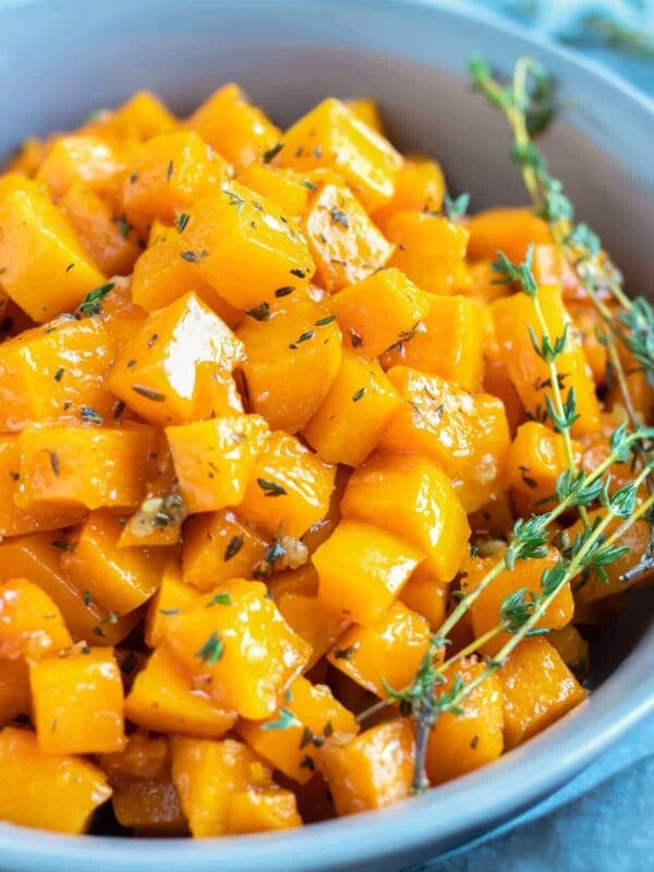 A serving bowl full of a roasted butternut squash recipe with maple syrup and fresh thyme.