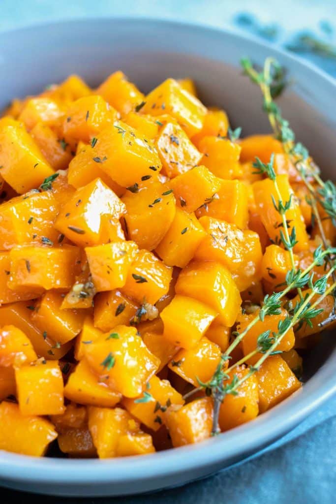 A serving bowl full of a roasted butternut squash recipe with maple syrup and fresh thyme.