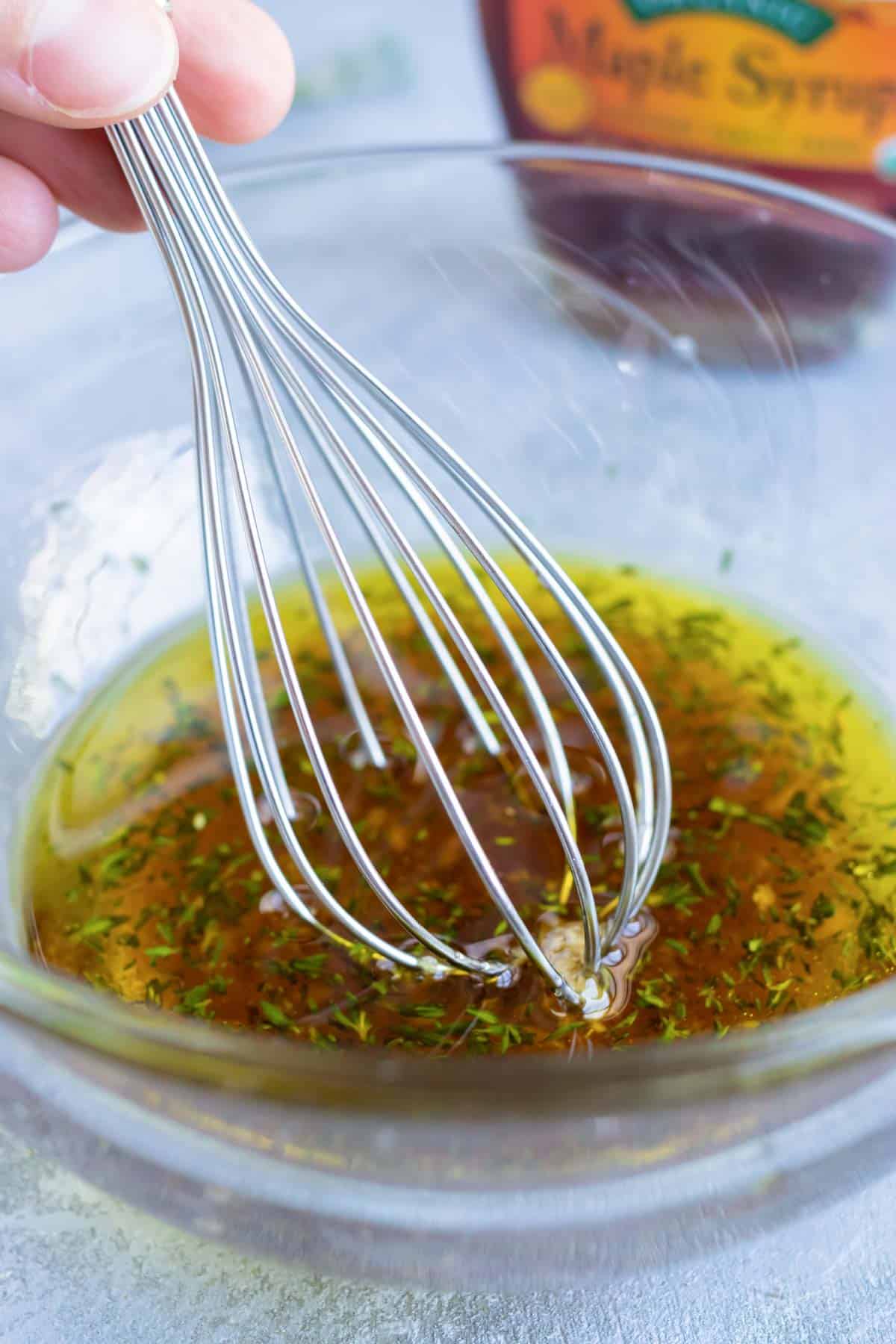 Whisking together a garlic maple and herb sauce in a small bowl.