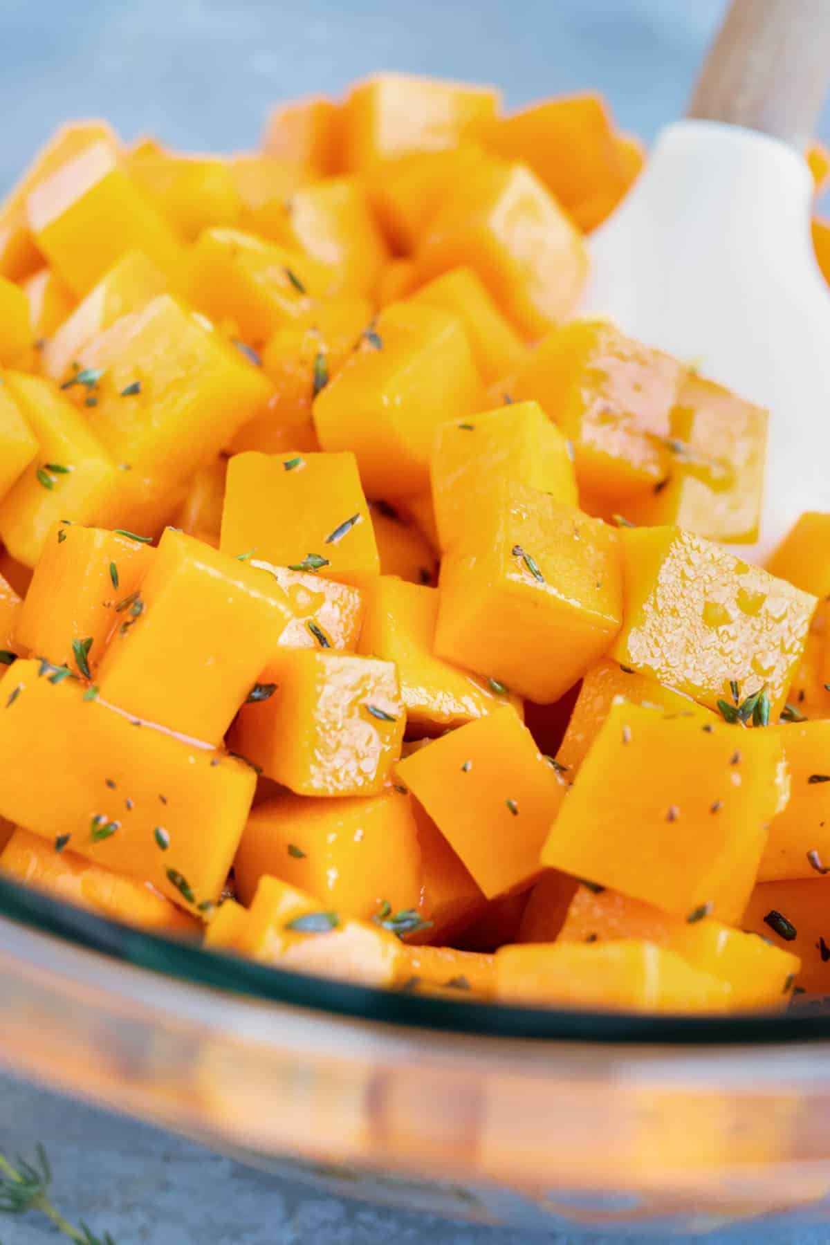 A spoon stirs seasoned butternut squash cubes.