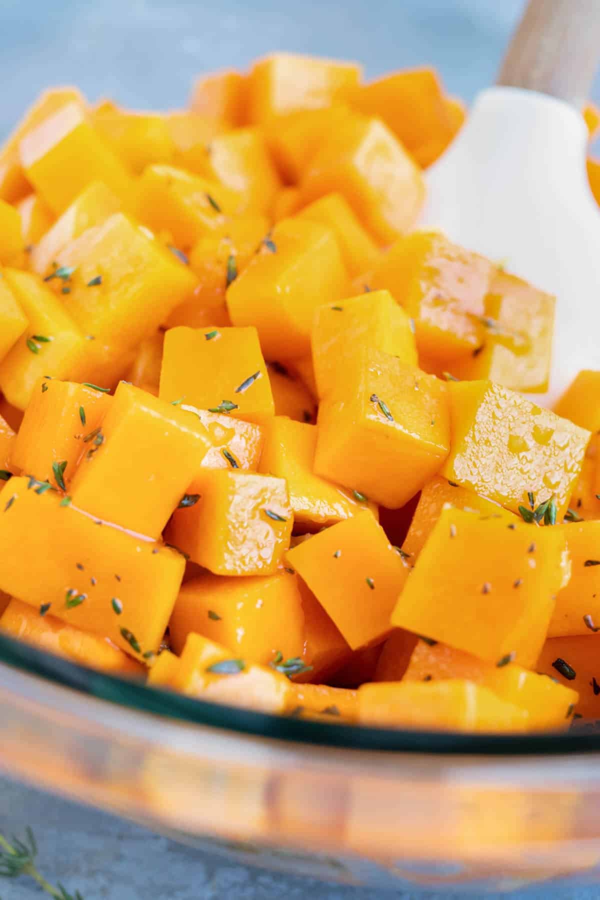 A spoon stirs seasoned butternut squash cubes.