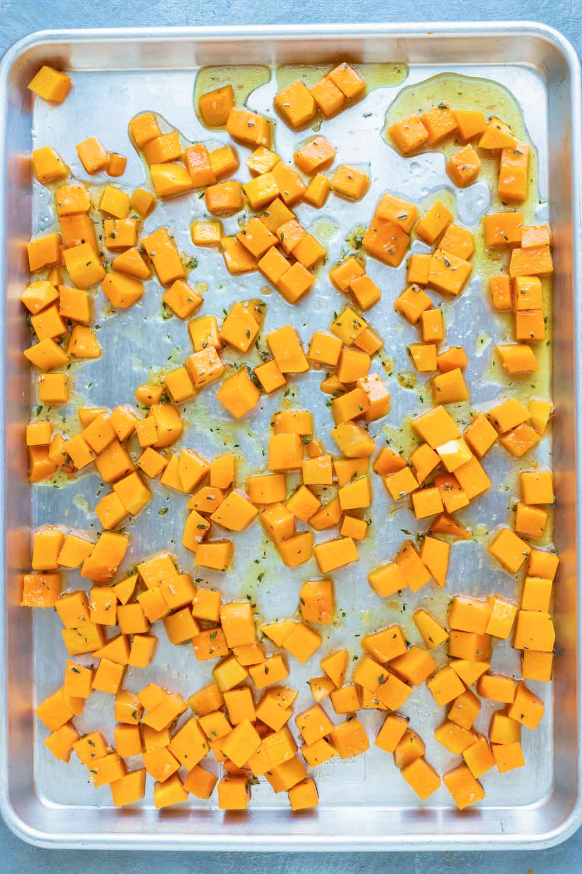 An image of roasted butternut squash cubes on a large baking sheet before baking.
