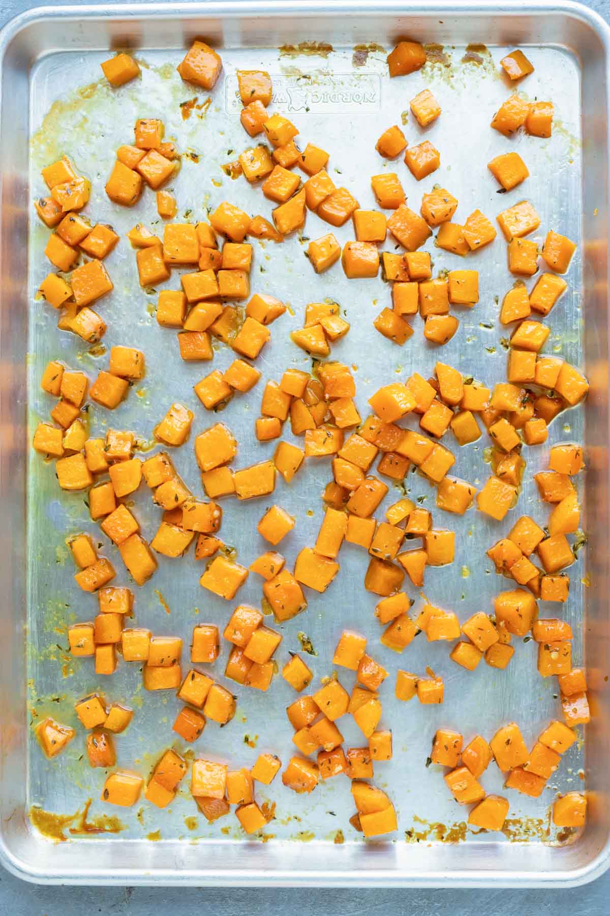 An image of roasted butternut squash cubes on a large baking sheet after baking.