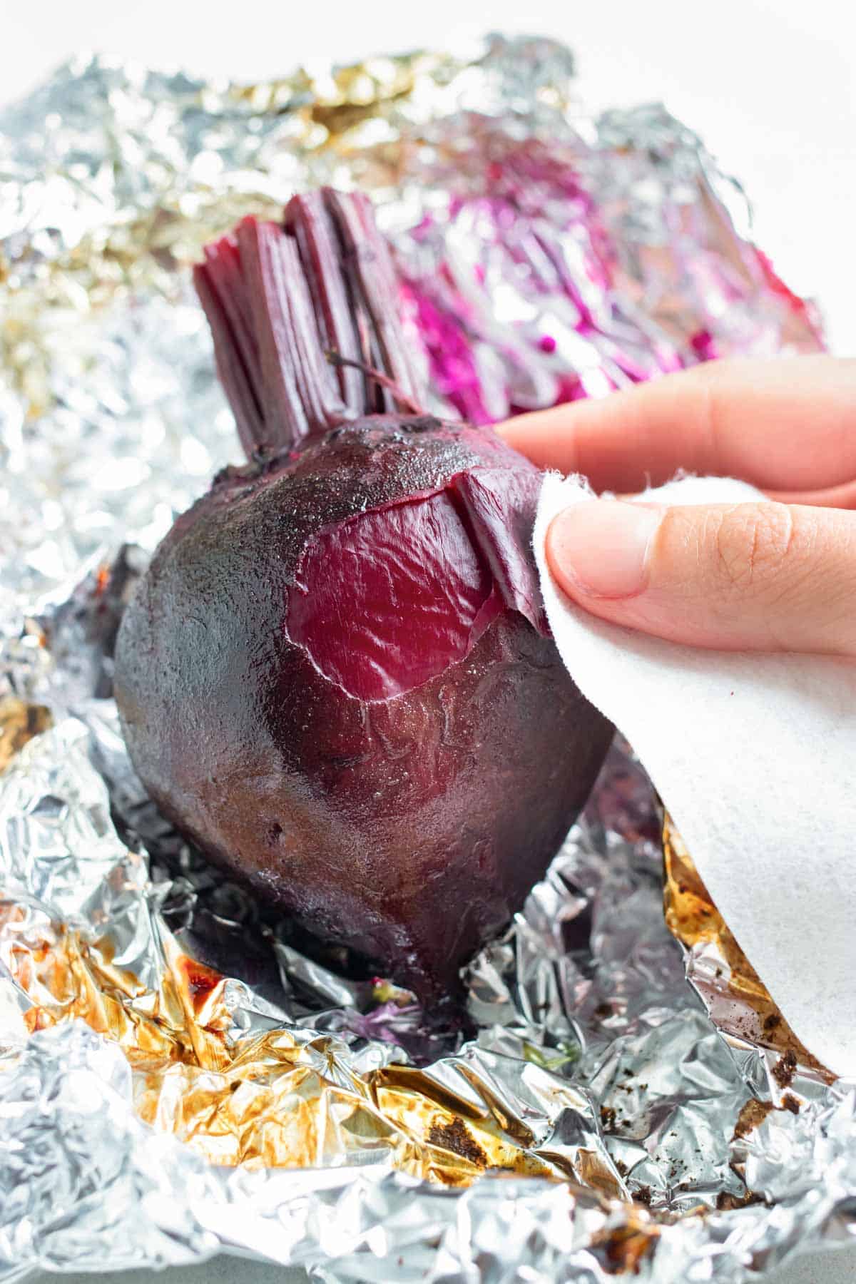 Baked beets are peeled using a paper towel after roasting in the oven.