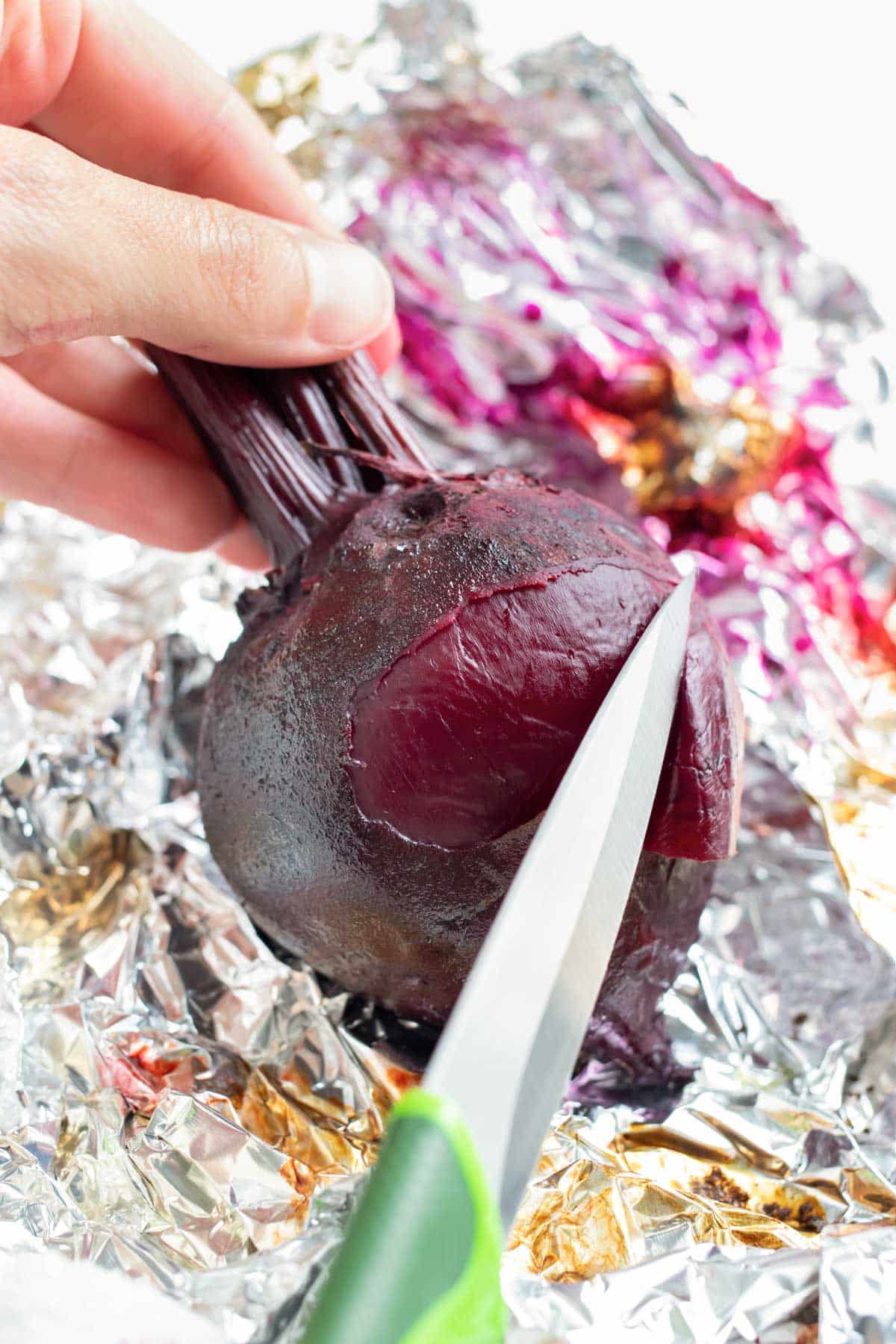 Beets roasted in the oven in aluminum foil are peeled with a pairing knife.