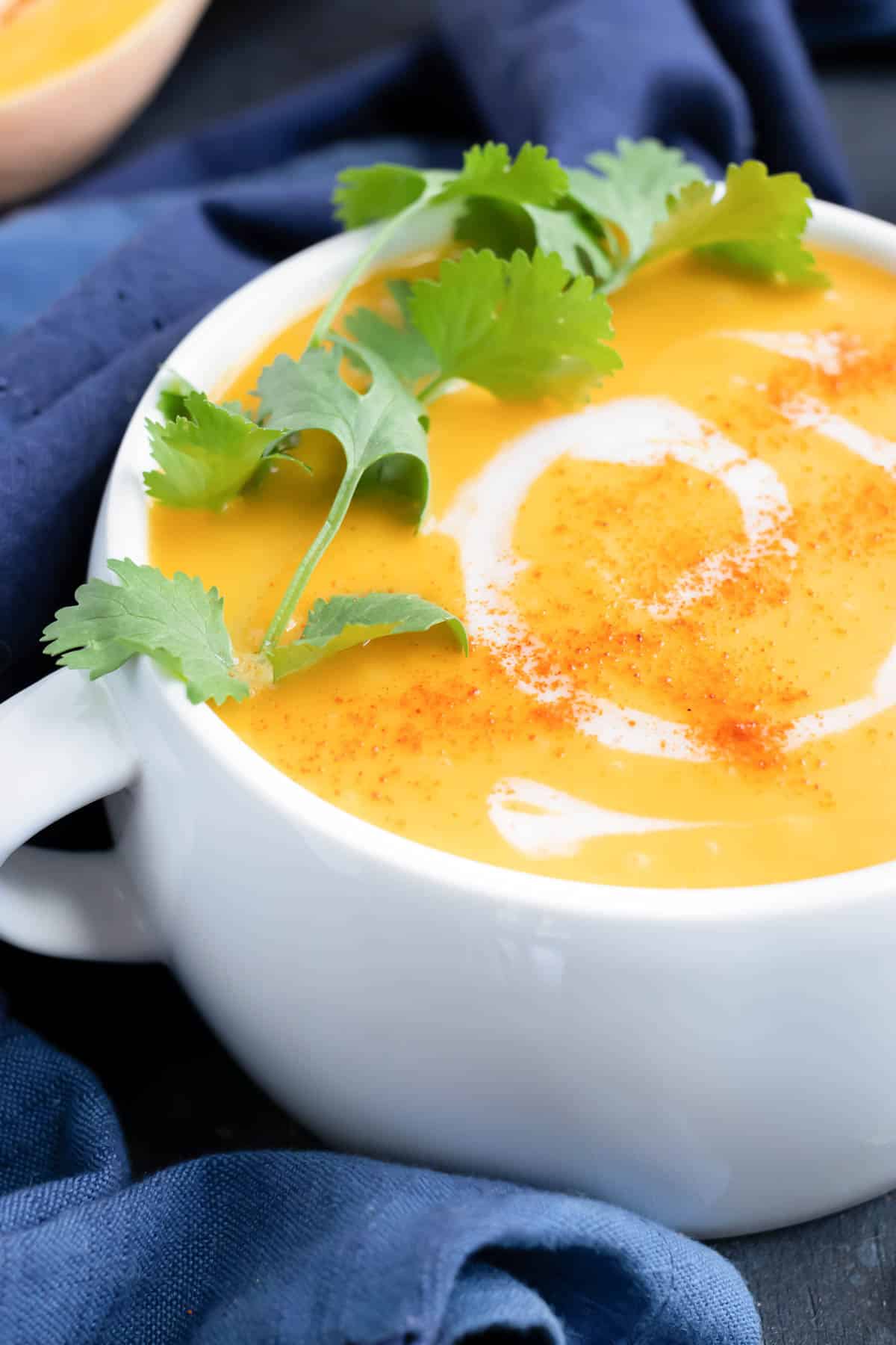 A healthy, Whole30, and Paleo butternut squash soup recipe that is in a white soup bowl with cilantro next to it.