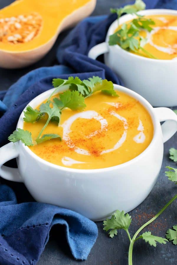 A serving bowl full of healthy, Paleo, Whole and vegan roasted butternut squash soup with a drizzle of coconut milk and a cilantro sprig on top.