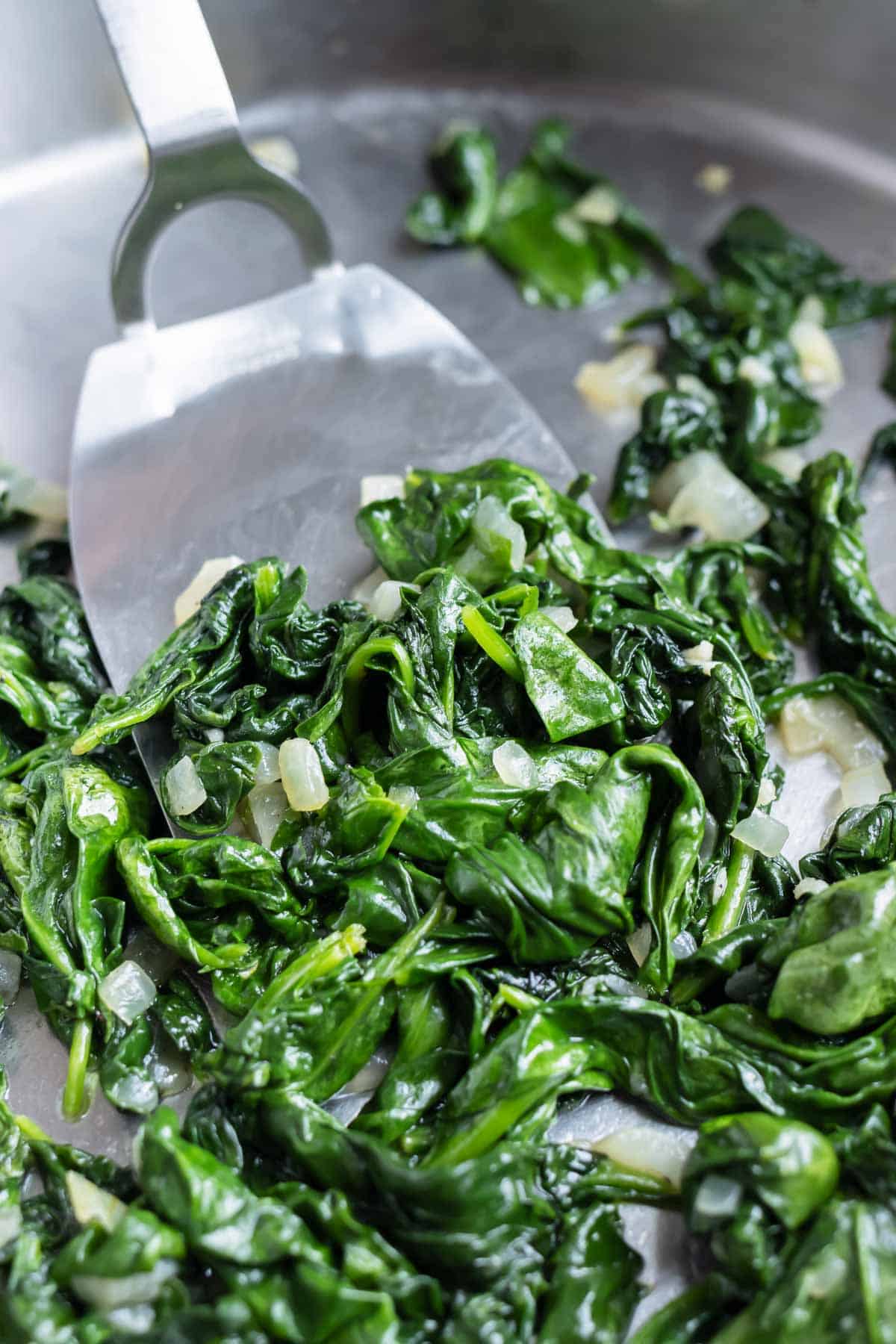 A spatula is used to dish the spinach from the pan.