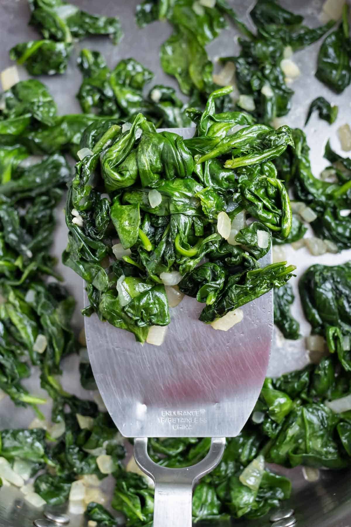 Spinach is sautéed on the stove in a pan.