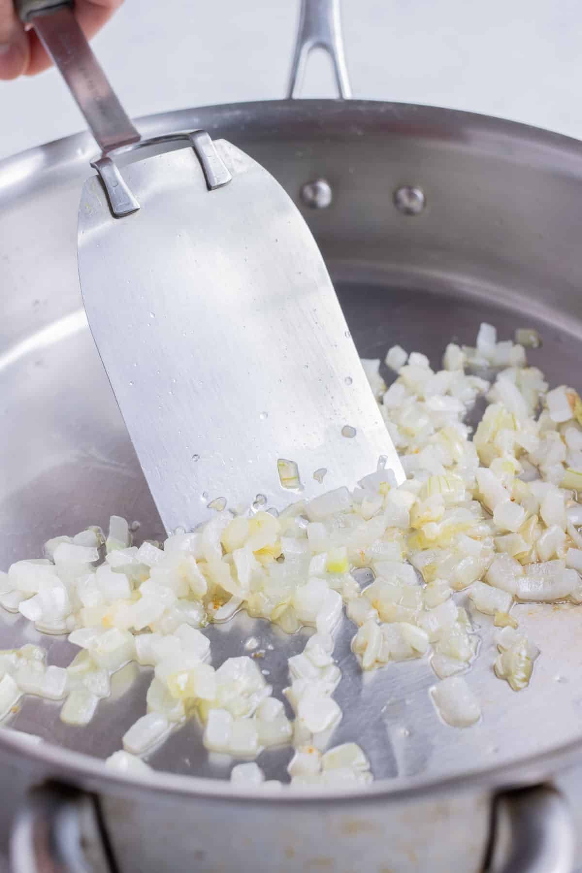 Diced onion and garlic are sautéed on the stove.