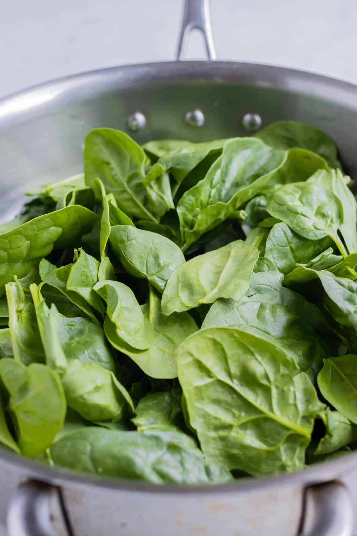 The spinach is added to the pan on the stove.