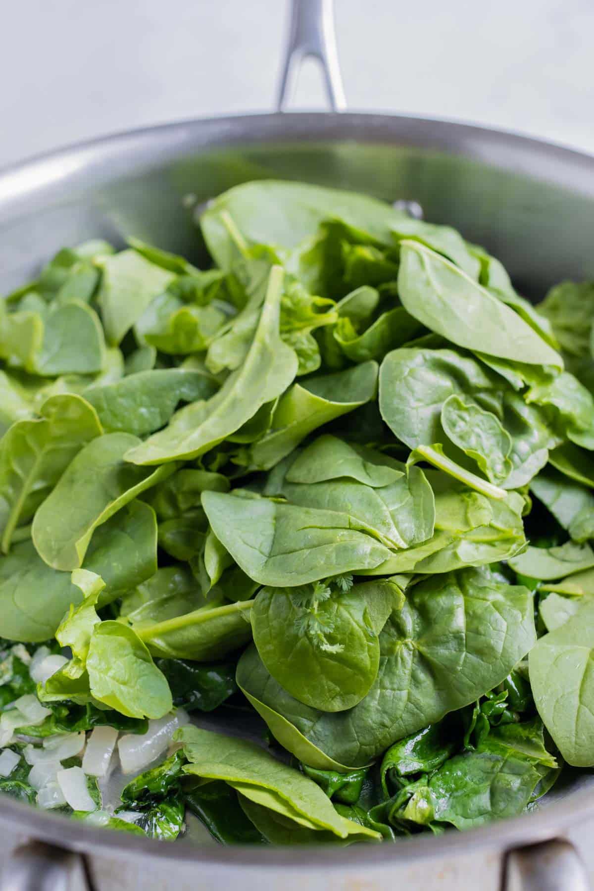 More fresh spinach is added to the pan.