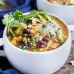 A big bowl of Crock-Pot chicken tortilla soup with corn, tomatoes, black beans, and cilantro on top.