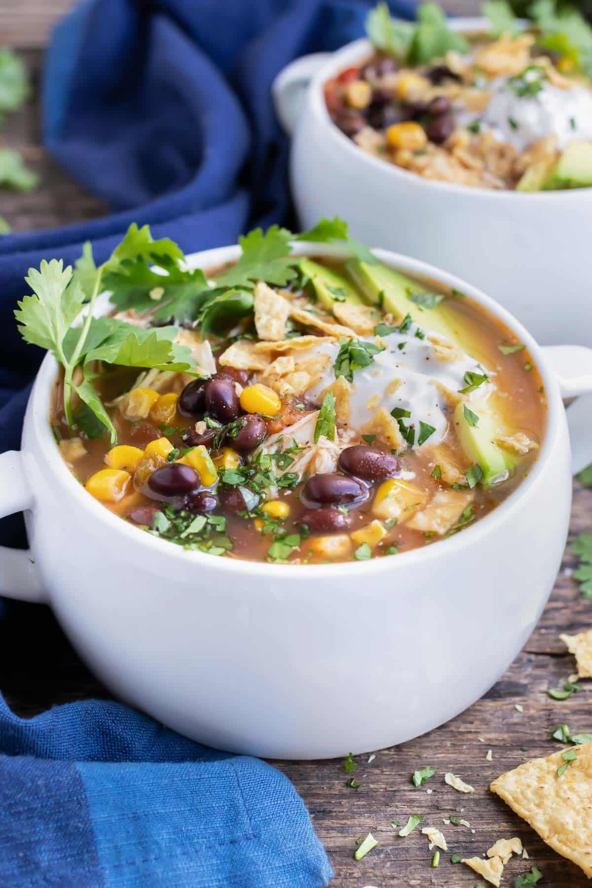 A big bowl of Crock-Pot chicken tortilla soup with corn, tomatoes, black beans, and cilantro on top.