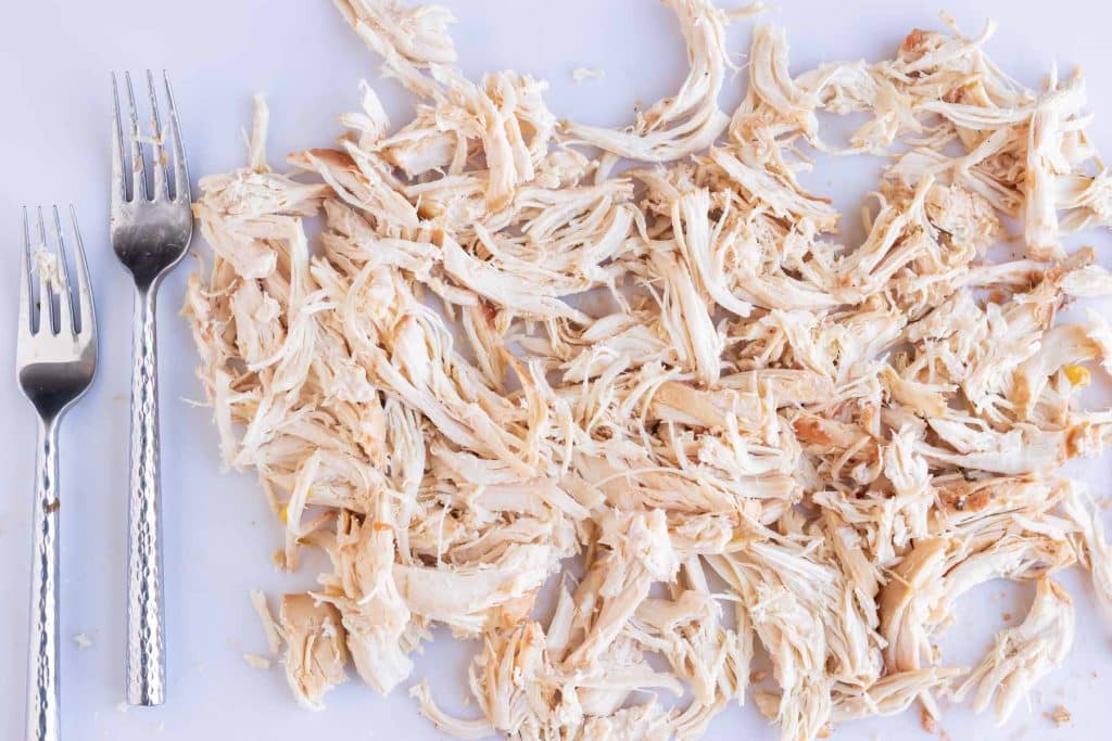 Two forks next to a pound of shredded chicken.