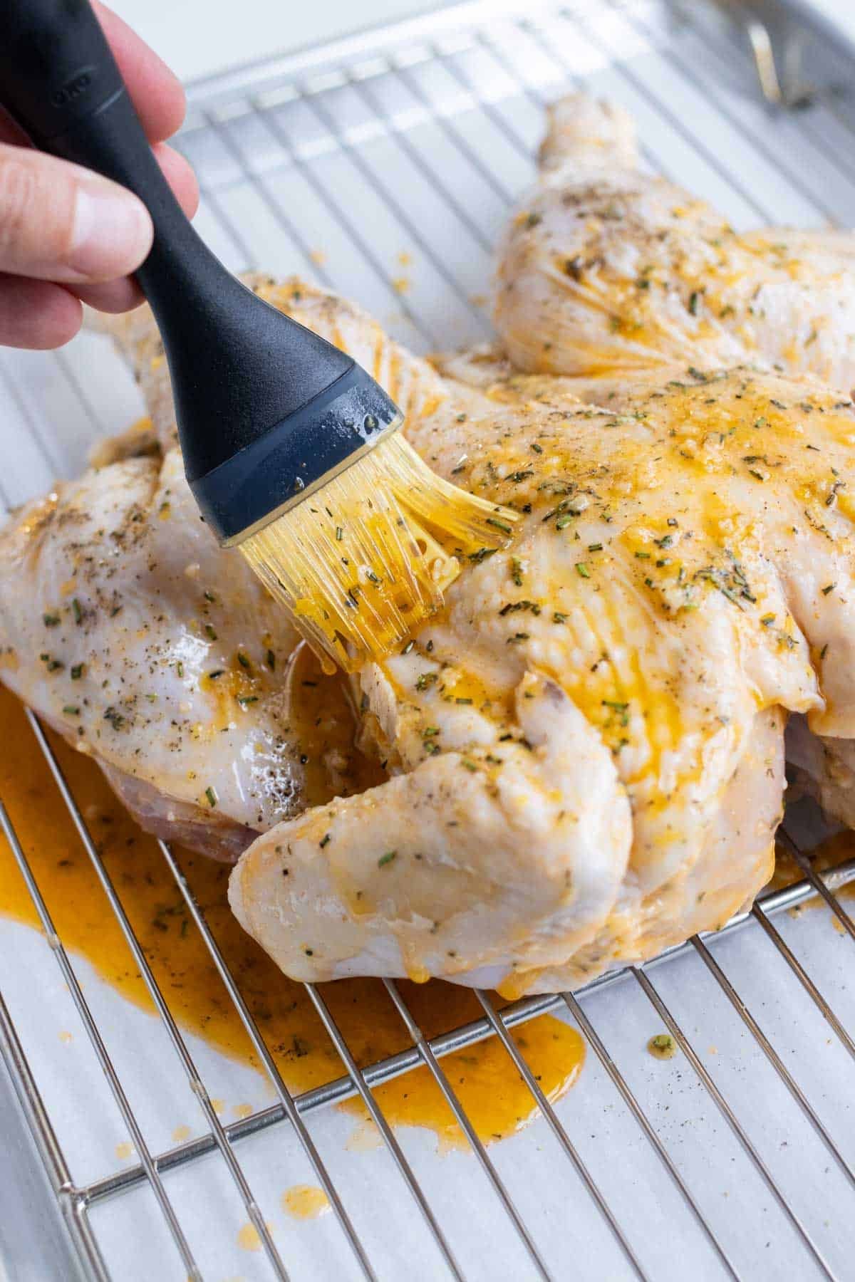 Melted, seasoned butter is brushed on the skin of a chicken.