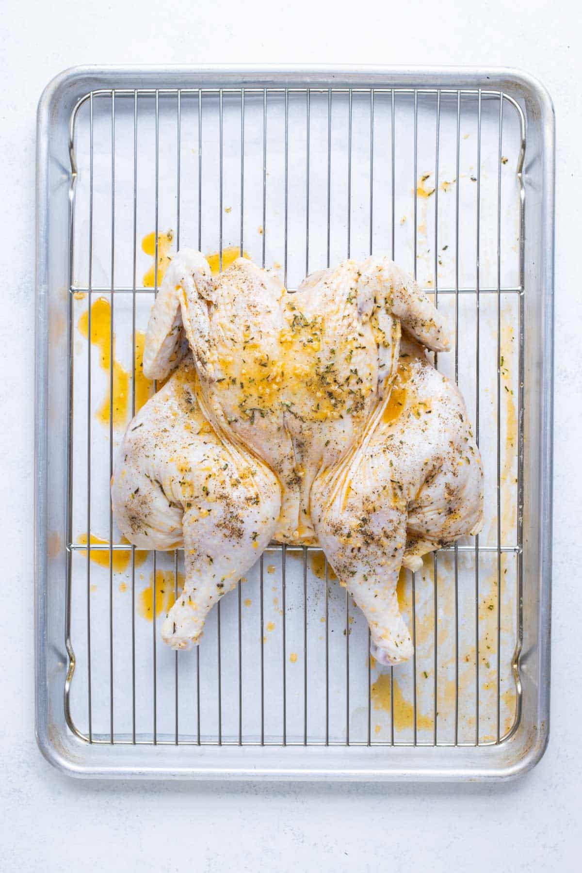 A seasoned spatchcock chicken sits on a rack on a baking sheet.