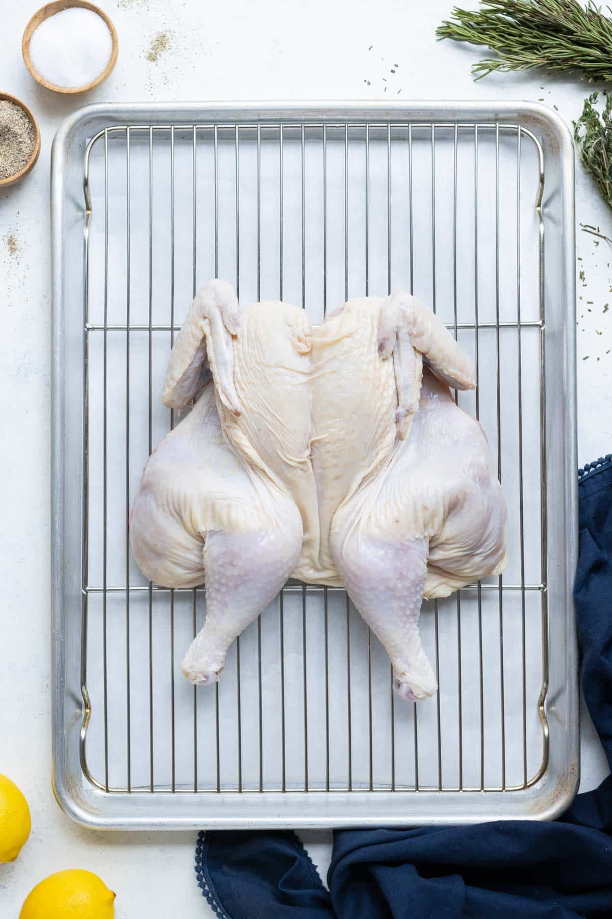 A baking dish with a wire rack has a spatchcock-cut chicken on it.