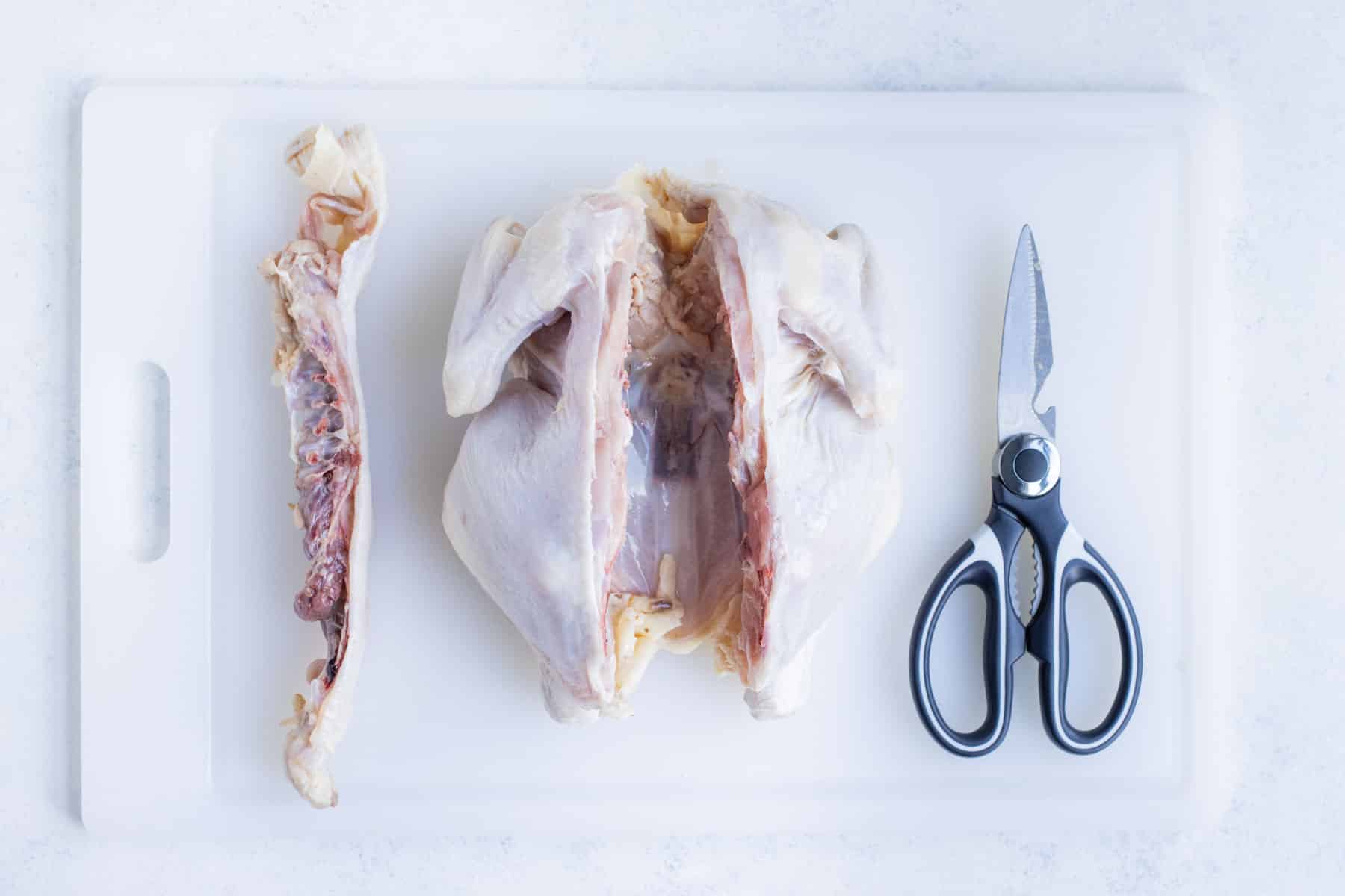 The spine is removed from a whole chicken with shears.