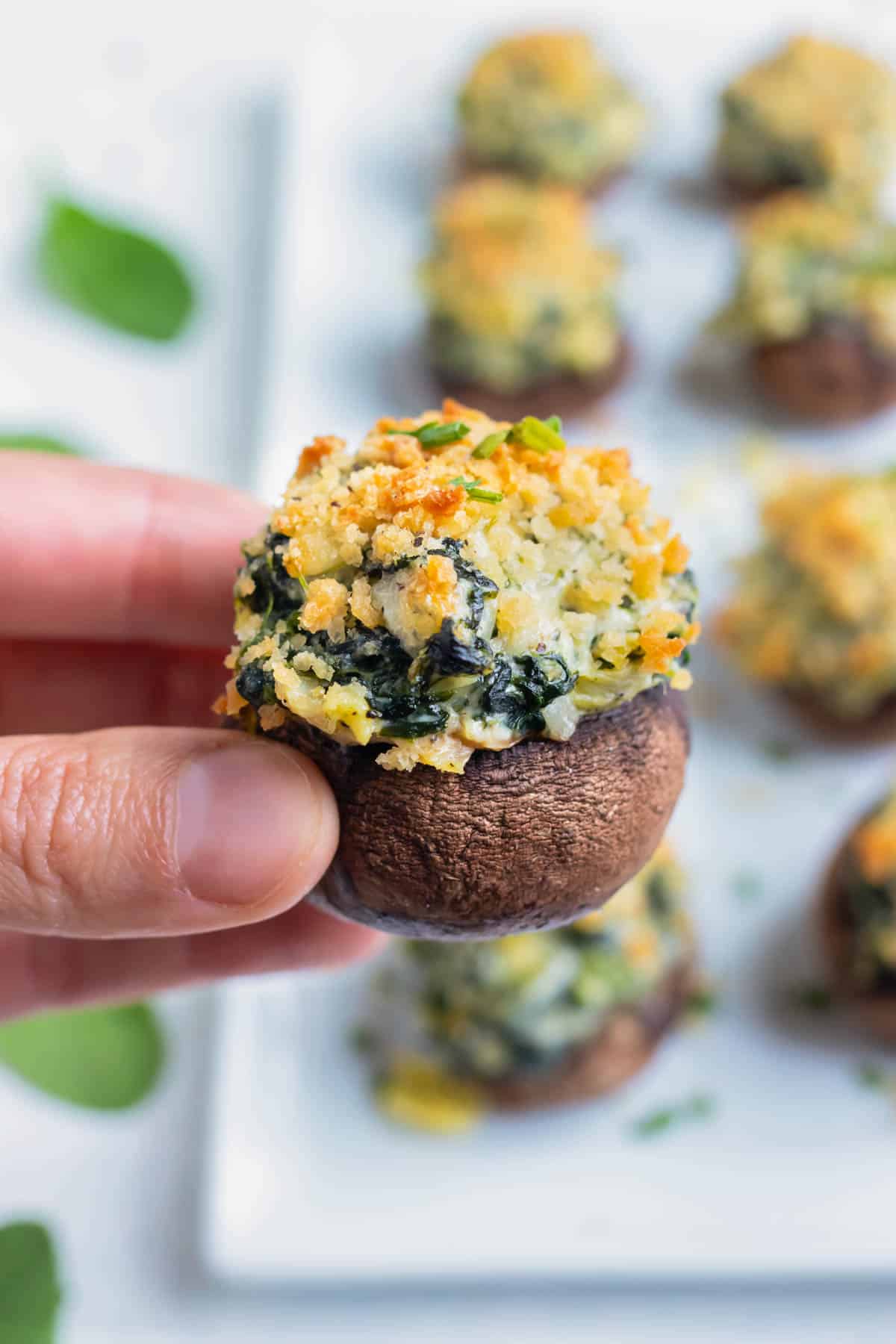 Spinach stuffed mushrooms are served with chives on a white platter.