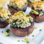 Low-carb spinach filled mushrooms are served on a white tray at a party.