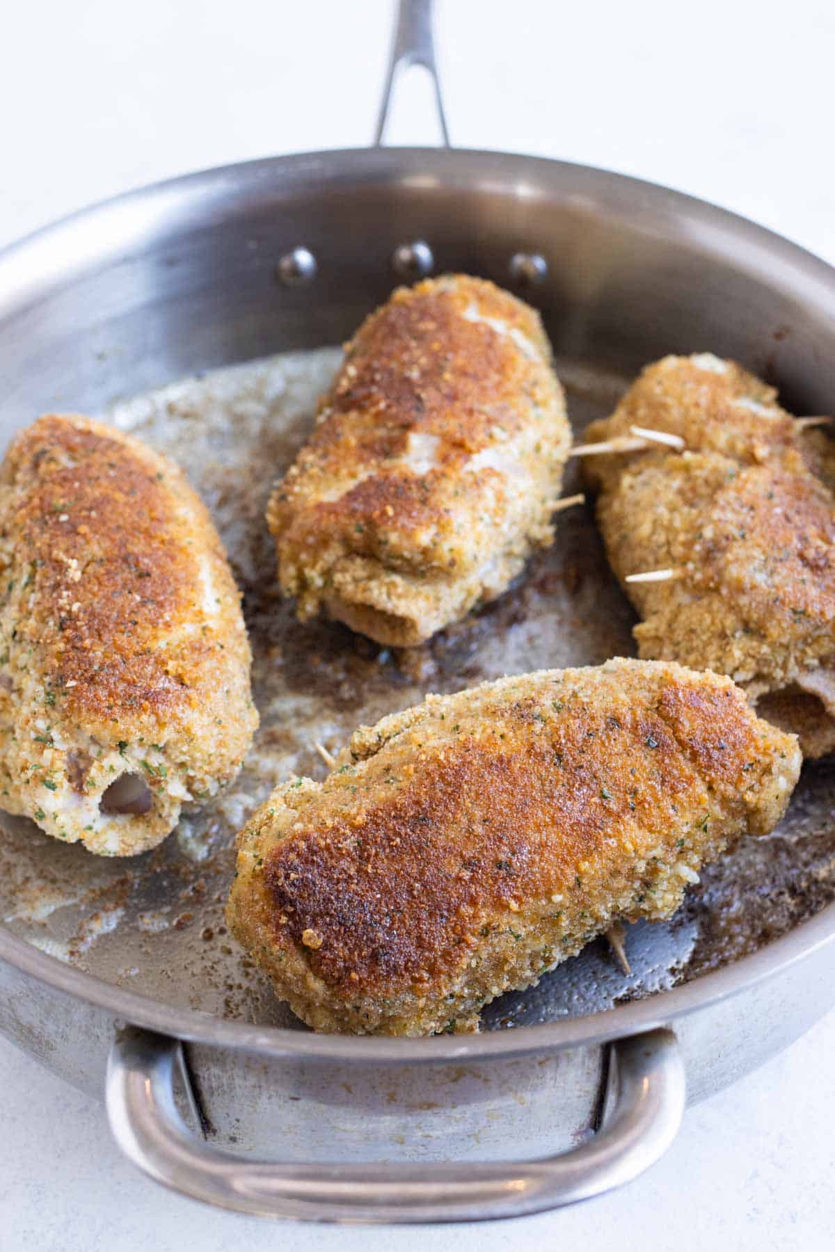 Four pieces of chicken rolled with ham and cheese are cooked in a skillet.