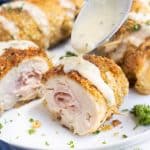 A creamy chicken cordon bleu sauce is drizzled onto a piece on a plate.