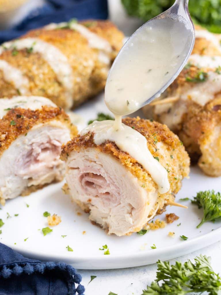 A creamy chicken cordon bleu sauce is drizzled onto a piece on a plate.
