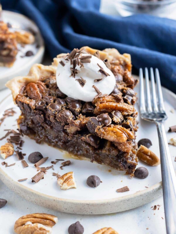 A slice of pecan pie with chocolate chips is shown on a plate with a fork.