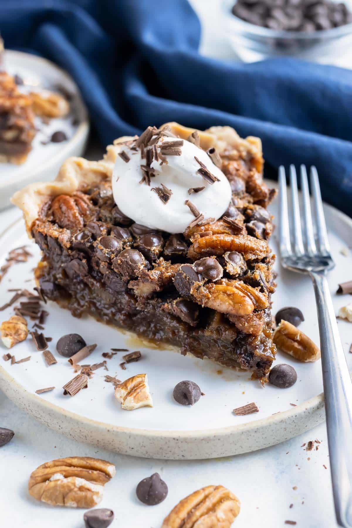 A slice of pecan pie with chocolate chips is shown on a plate with a fork.