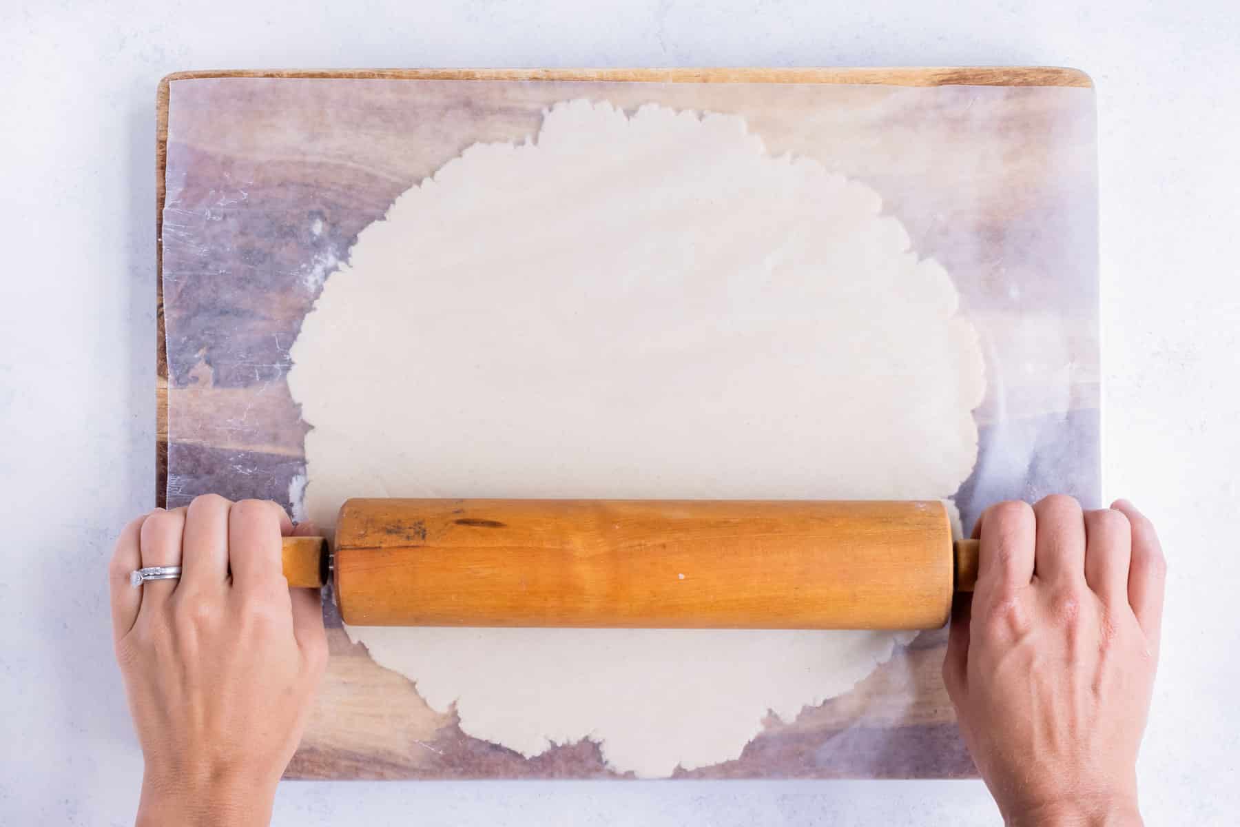 Pie dough is rolled out on a floured surface with wax paper over the dough.