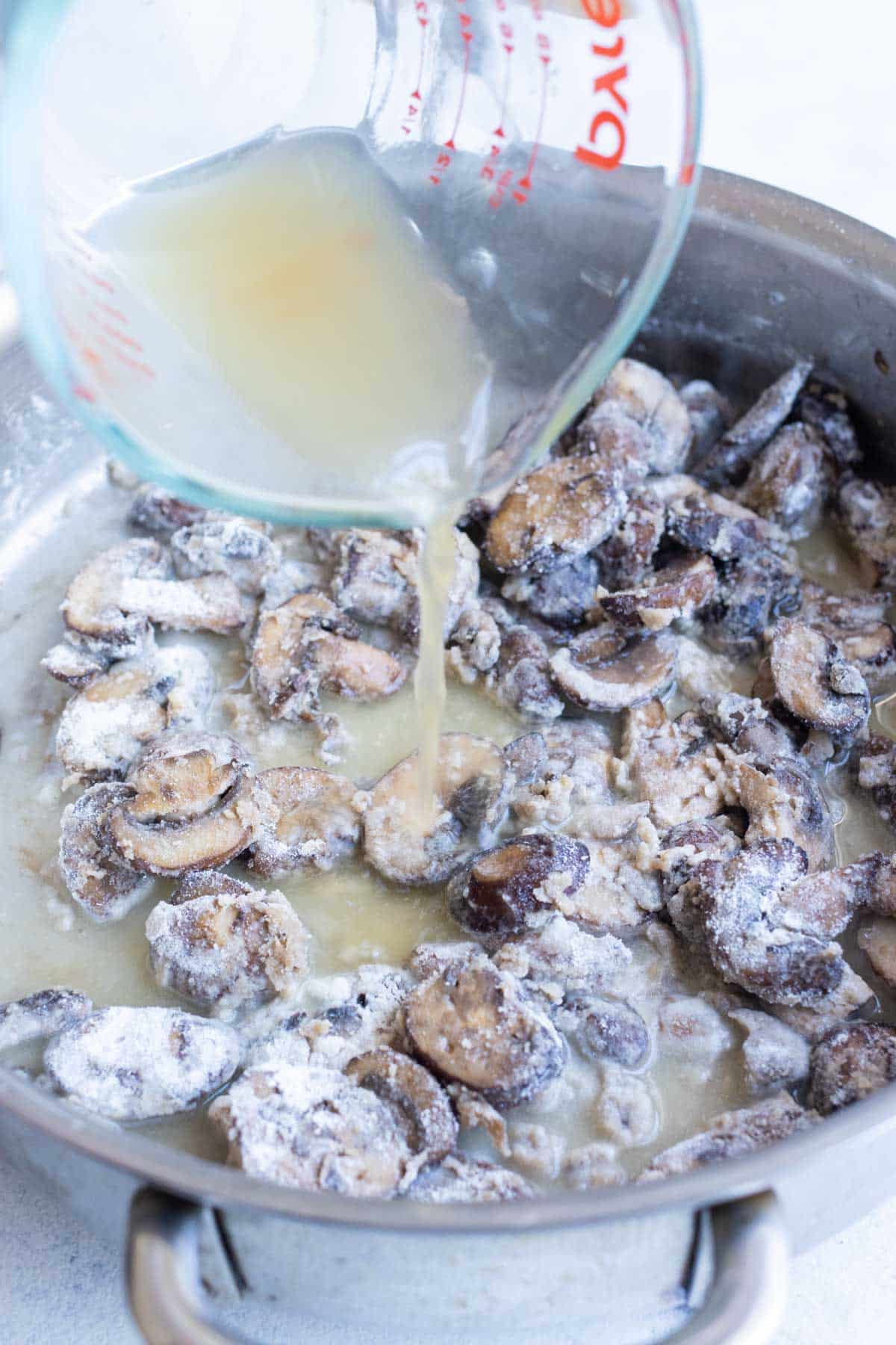 Broth is poured into sauteed mushrooms in a skillet.