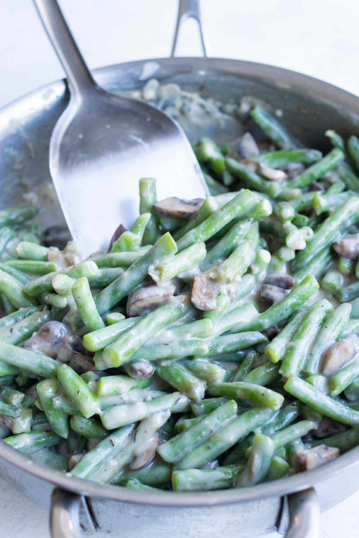 Green beans are added to a skillet with a dairy-free cream of mushroom soup.